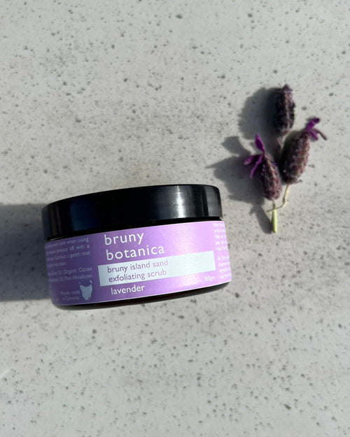 Jar of Bruny Island Sand Exfoliating Body Scrub - Lavender on a concrete surface with a sprig of lavender.