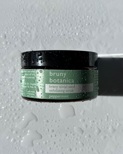 Jar of Bruny Botanica Peppermint body scrub on a textured marble background with water droplets