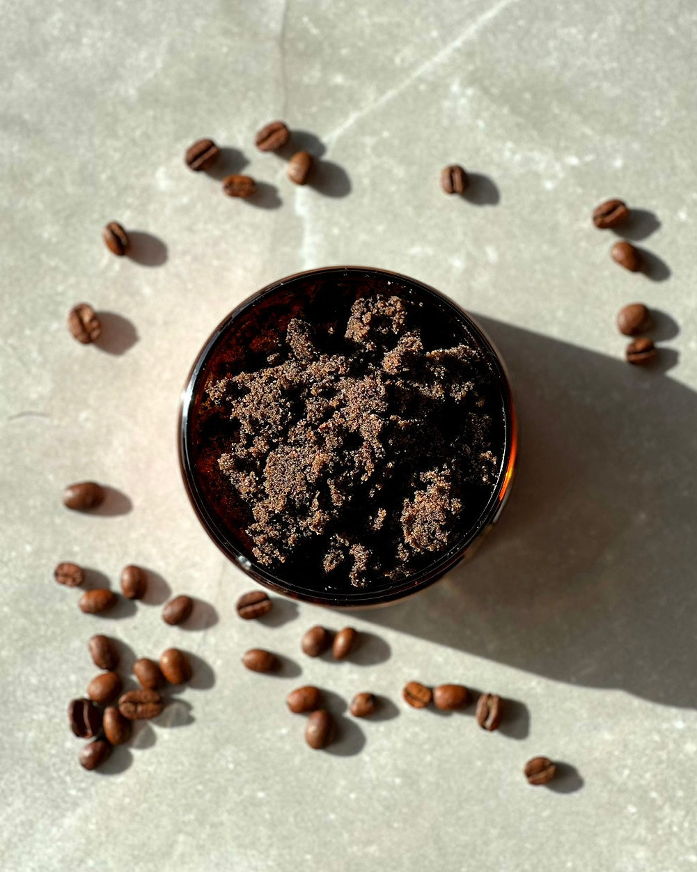 An overhead image of a Bruny Island Sand Exfoliating Body Scrub - Coffee with scattered coffee beans on a textured surface