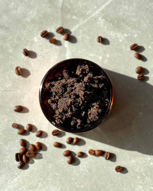An overhead image of a Bruny Island Sand Exfoliating Body Scrub - Coffee with scattered coffee beans on a textured surface