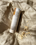 Bruny Botanics Coconut & Oat Magnesium Bath Soak tube on a textured beige fabric background with scattered oats.