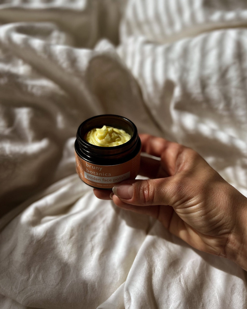 Hand holding a jar of Golden Face Polish on a textured white surface
