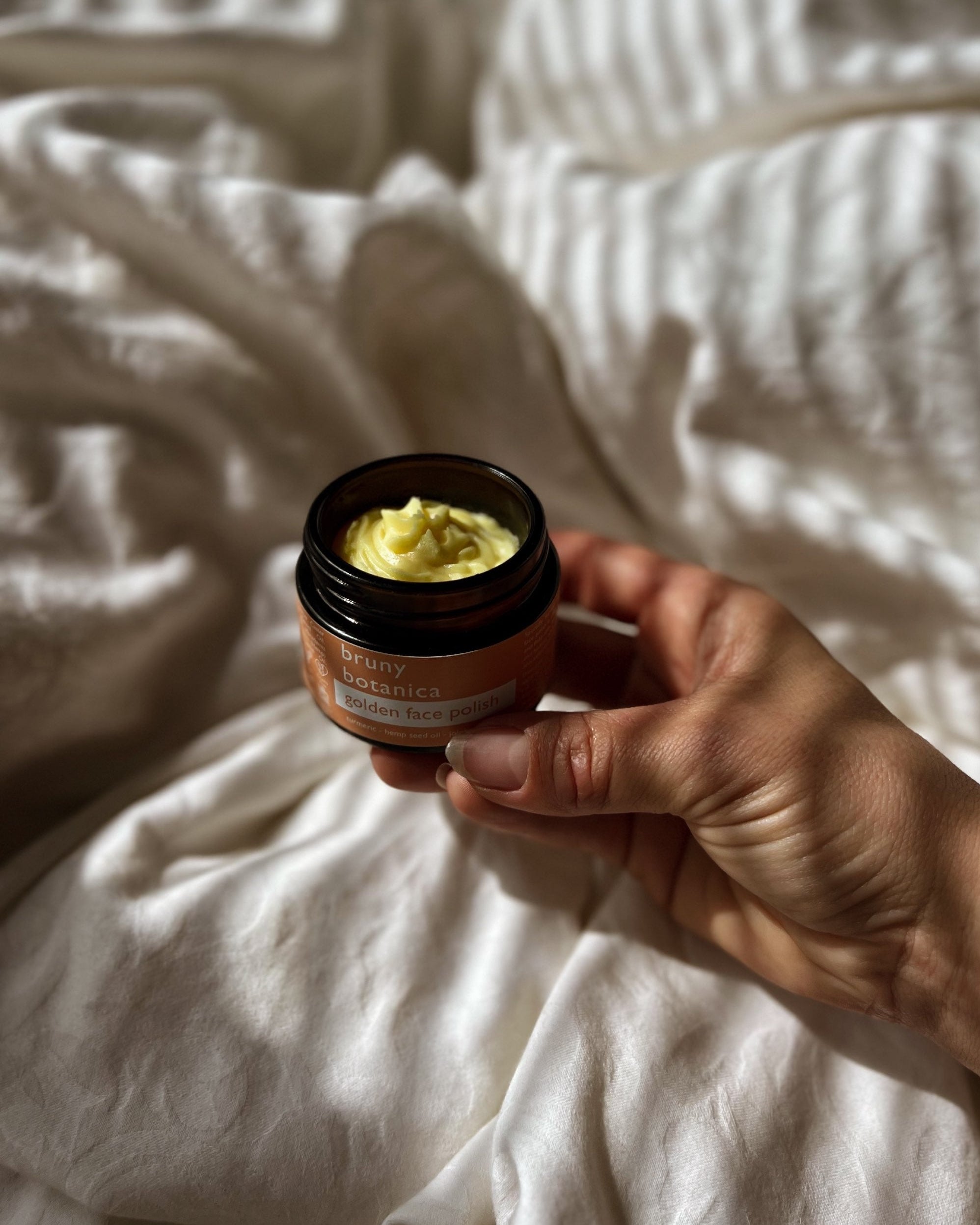 Hand holding a jar of Golden Face Polish on a textured white surface