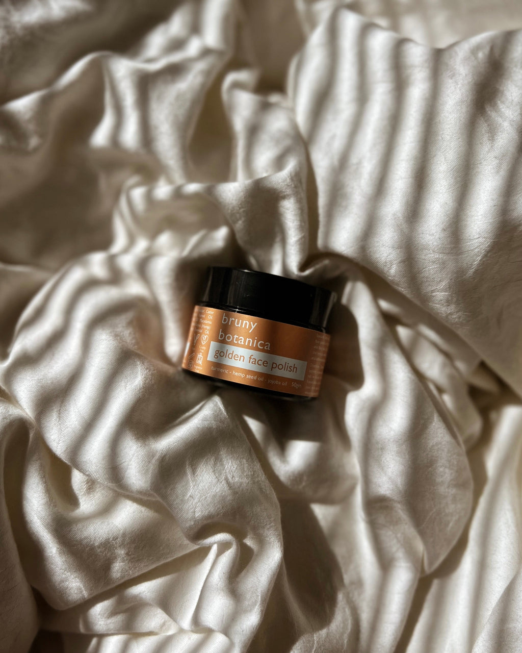 Jar of Golden Face Polish on a textured white fabric surface
