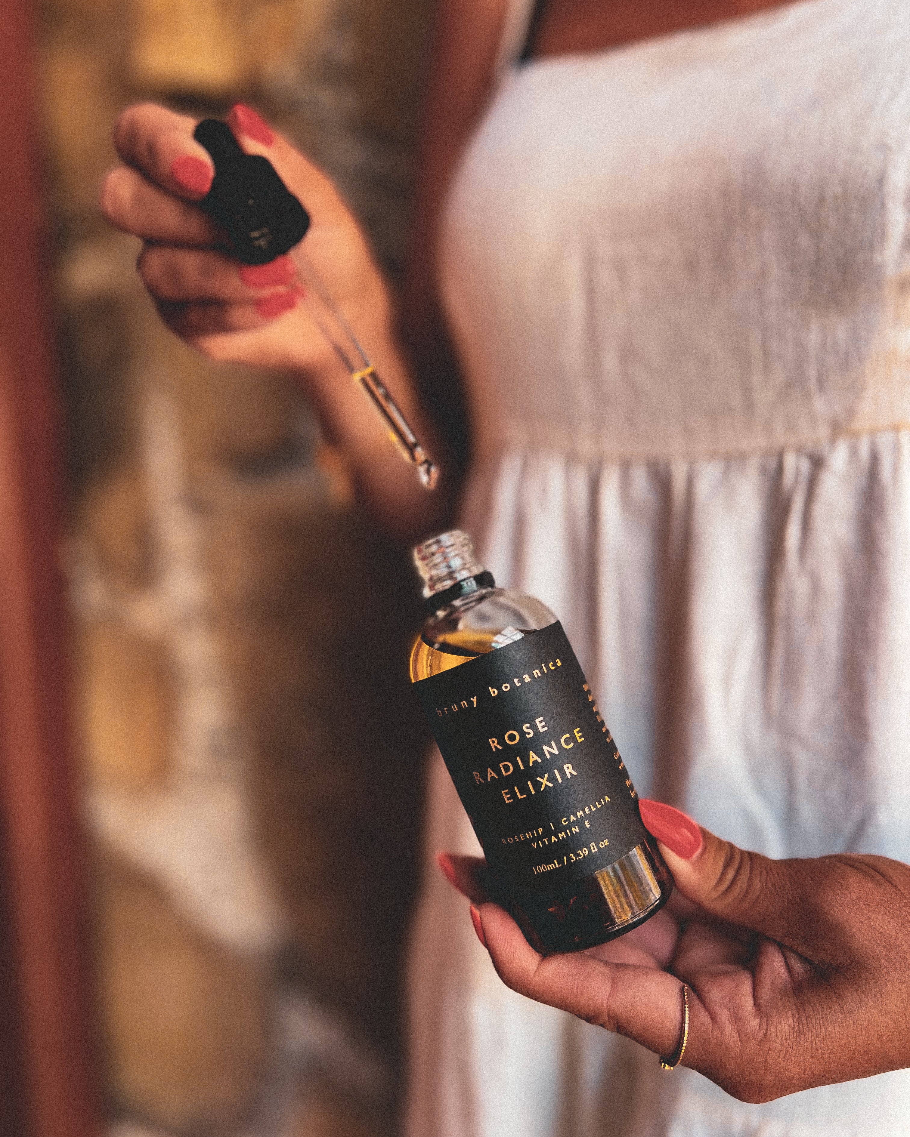 Bottle of 'Rose Radiance Elixir' with the dropper held by a person.