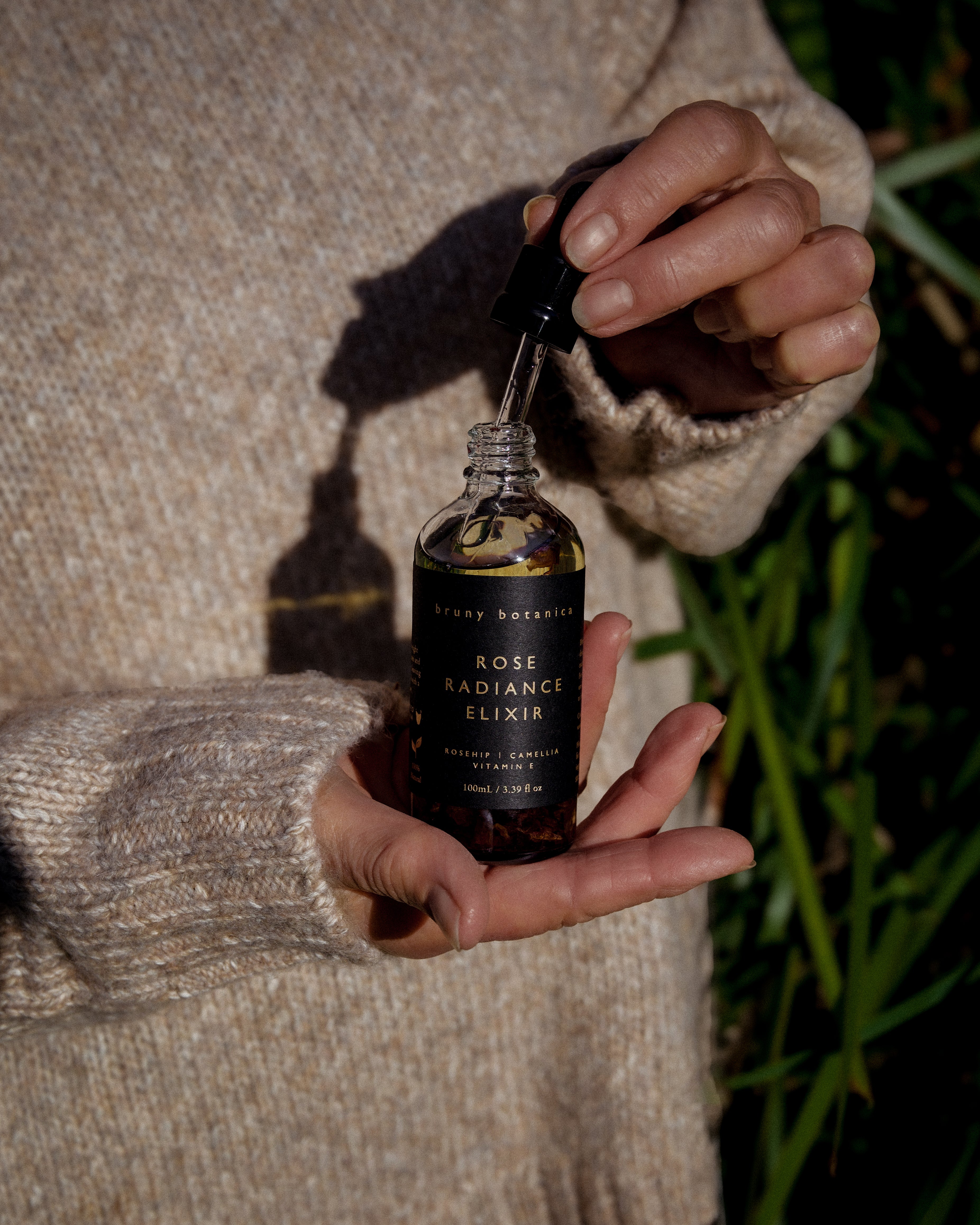 Rose Radiance Elixir Body Oil being held, with the dropper slightly lifted from the bottle
