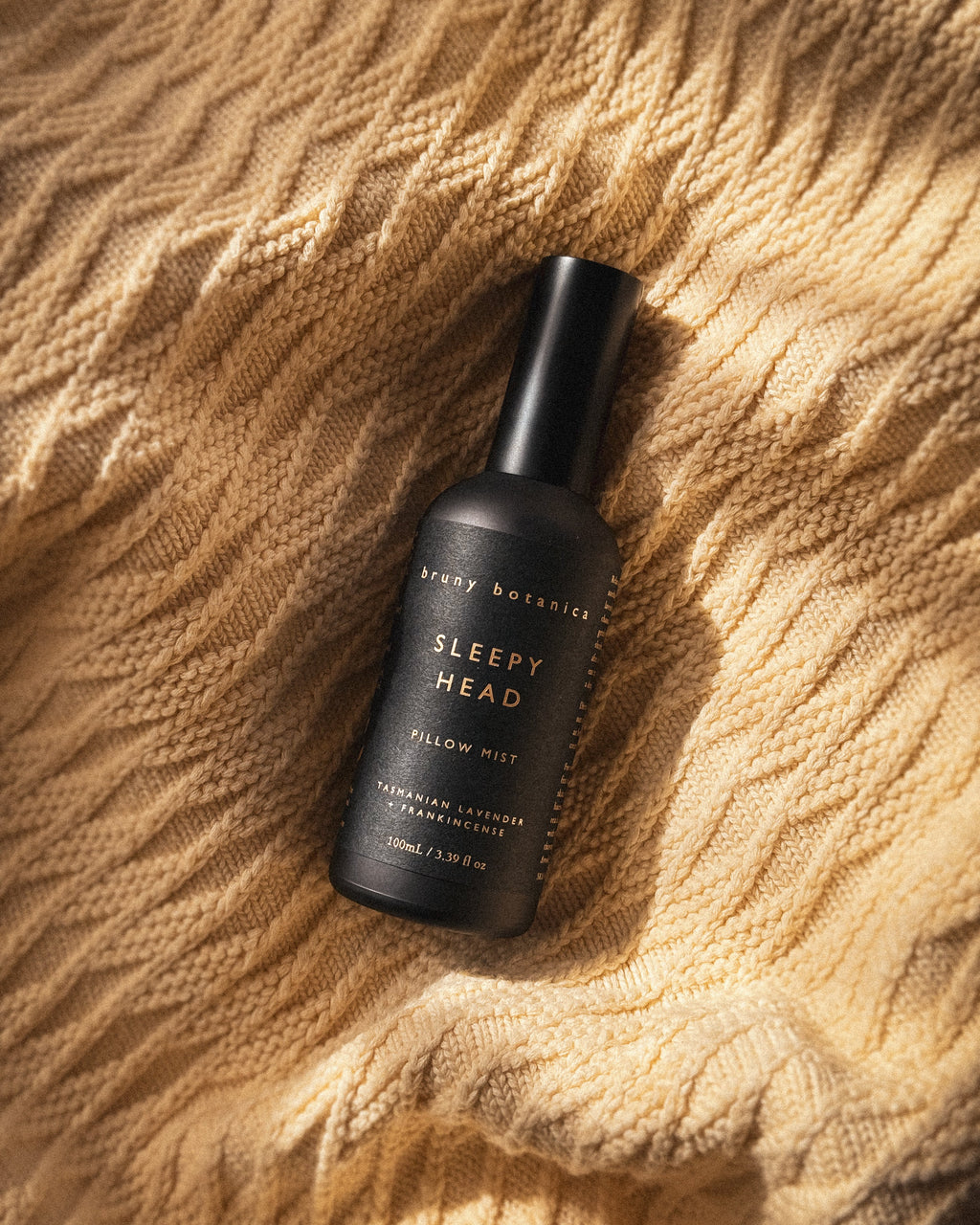 Black bottle of 'Sleepy Head' pillow mist on a textured beige surface