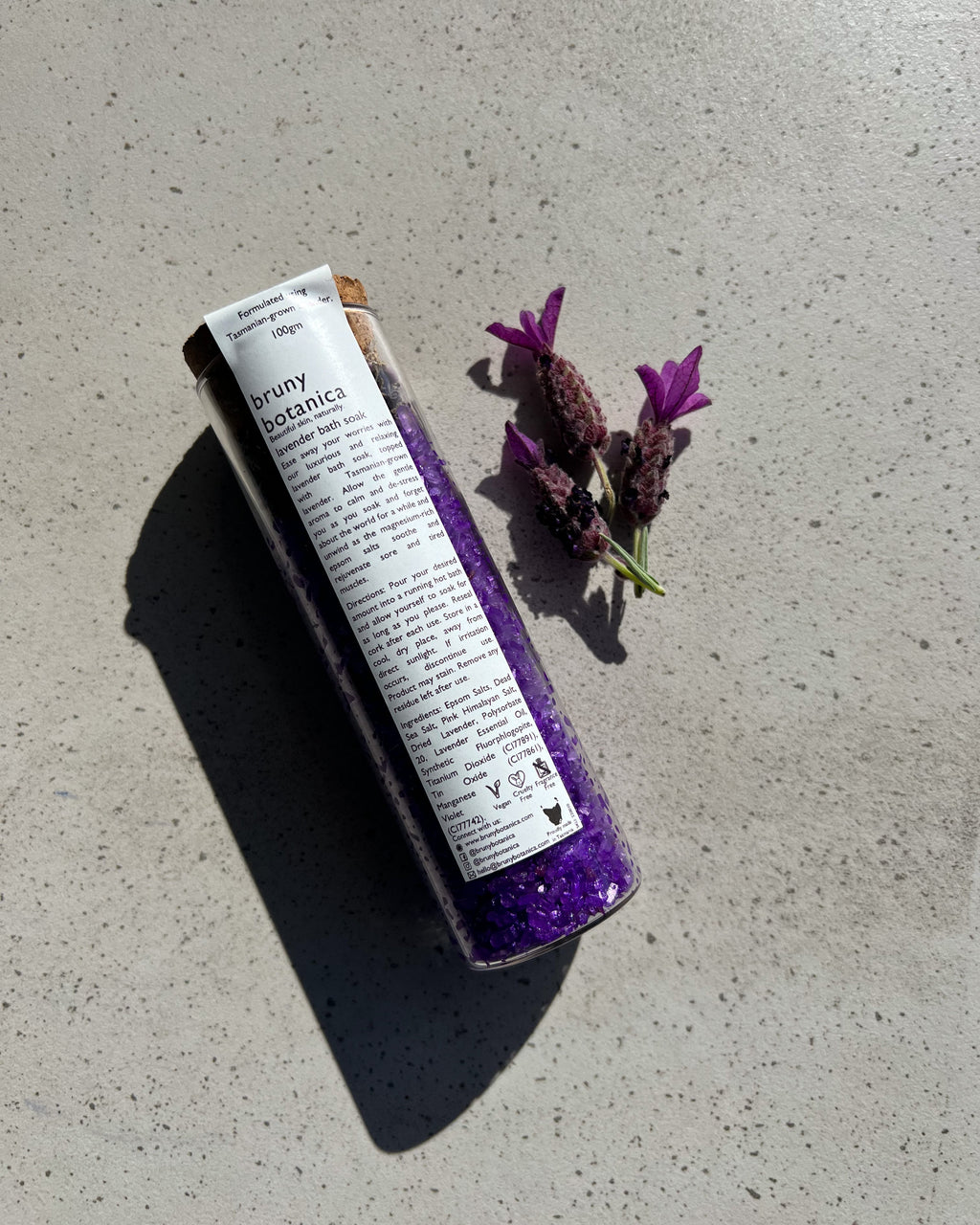 A tube of Tasmanian Lavender Magnesium Bath Soak on a concrete surface next to a small bundle of lavender.