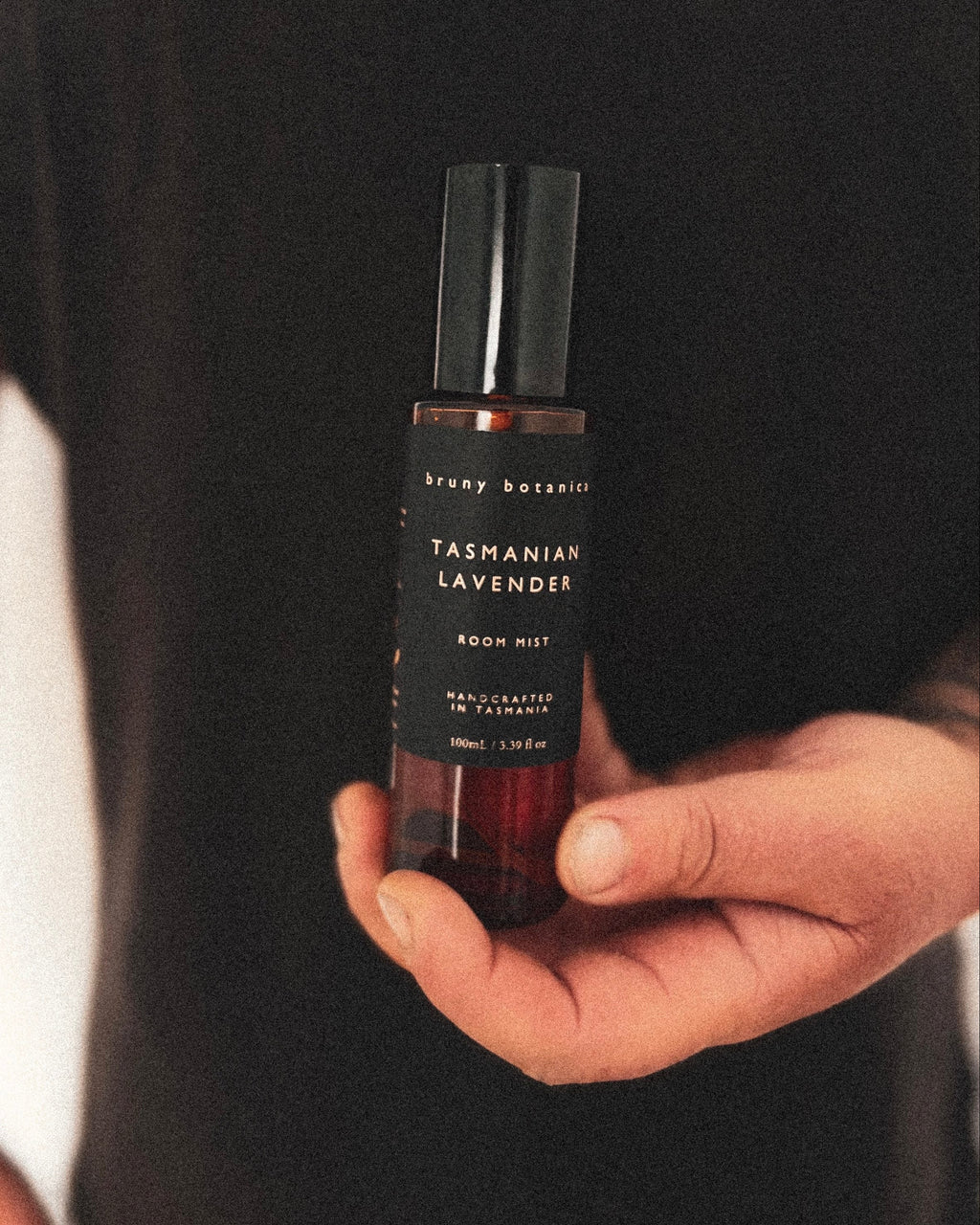 Person holding a bottle of Tasmanian Lavender room mist against a black background
