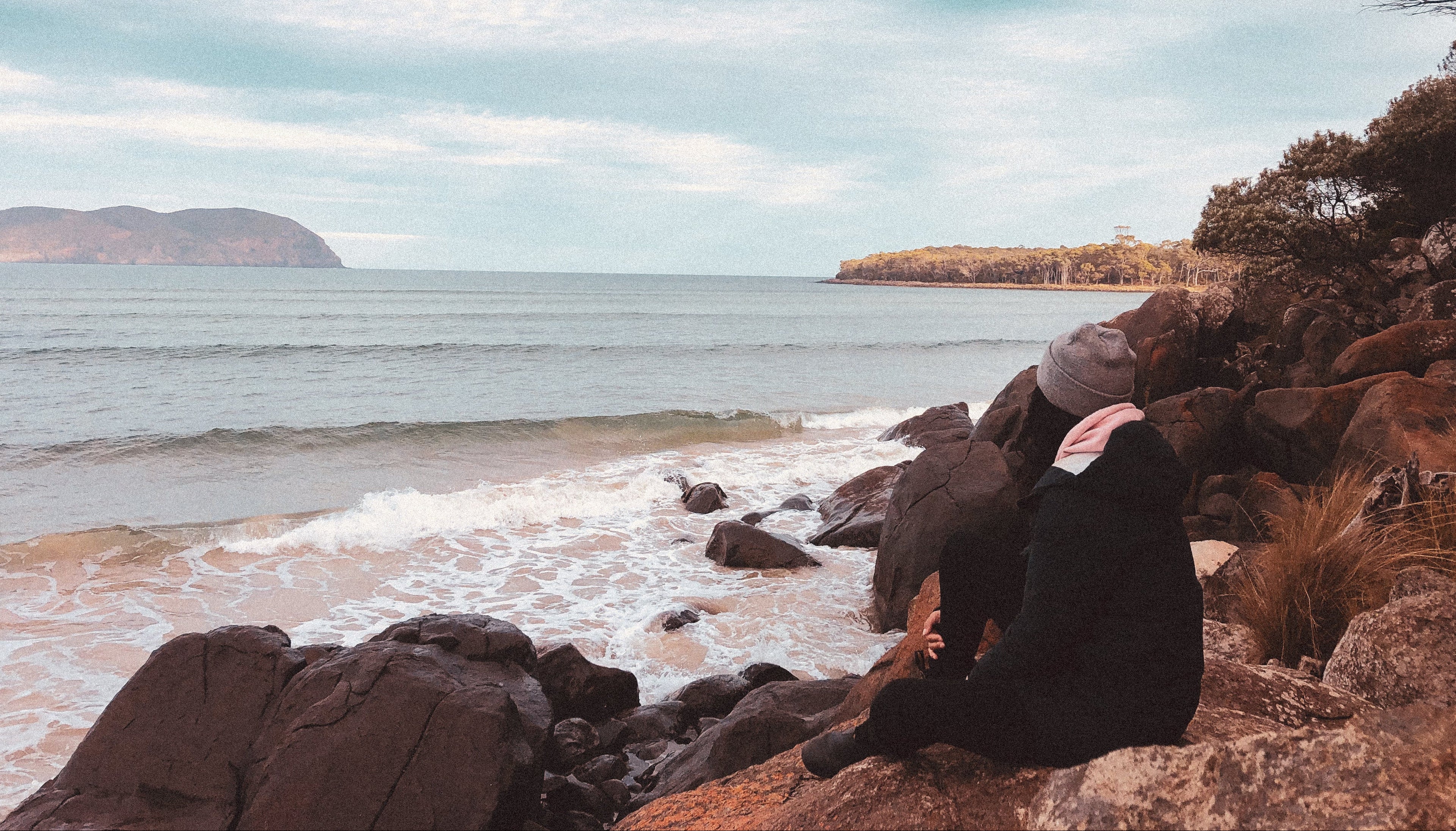 Person sitting on rocks by the ocean with a scenic view