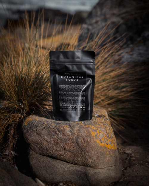 Black packaging of the Bruny Botanica botanical scrub on a rock with grass in the background