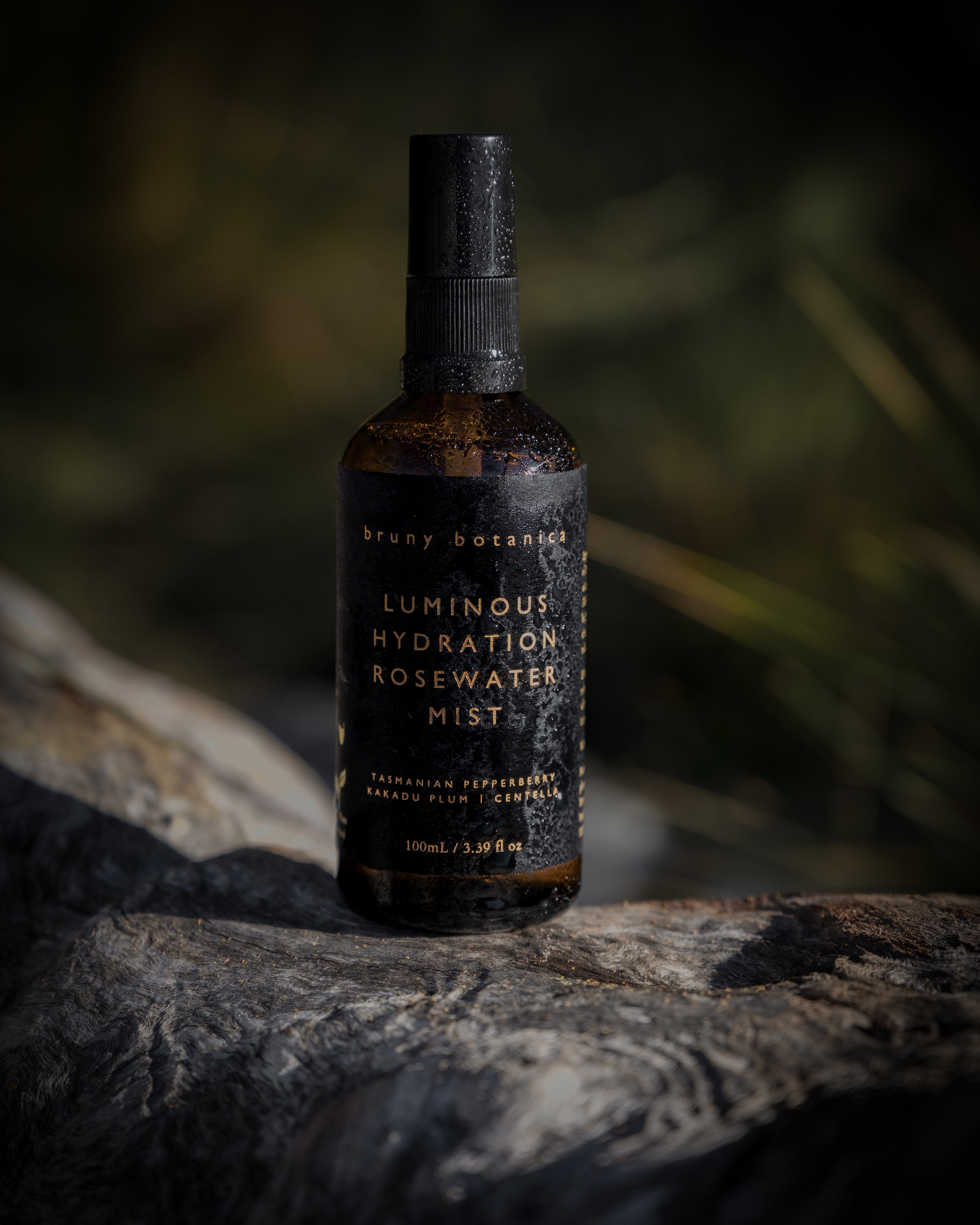 Bottle of 'Luminous Hydration Rosewater Mist' on a stone surface with a blurred natural background