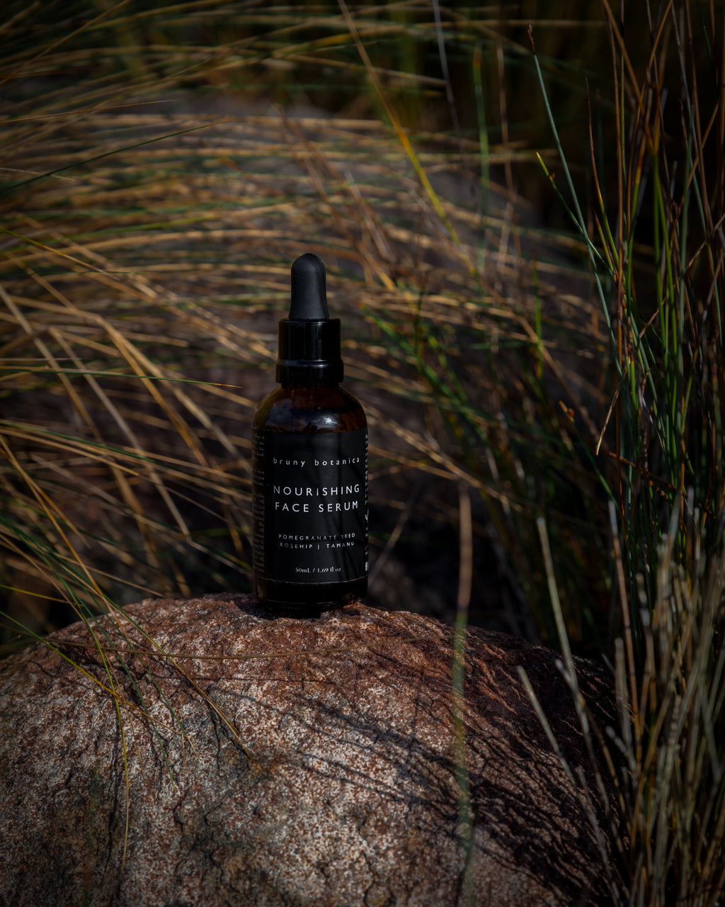 Bottle of Nourishing Face Serum on a rock with grass in the background