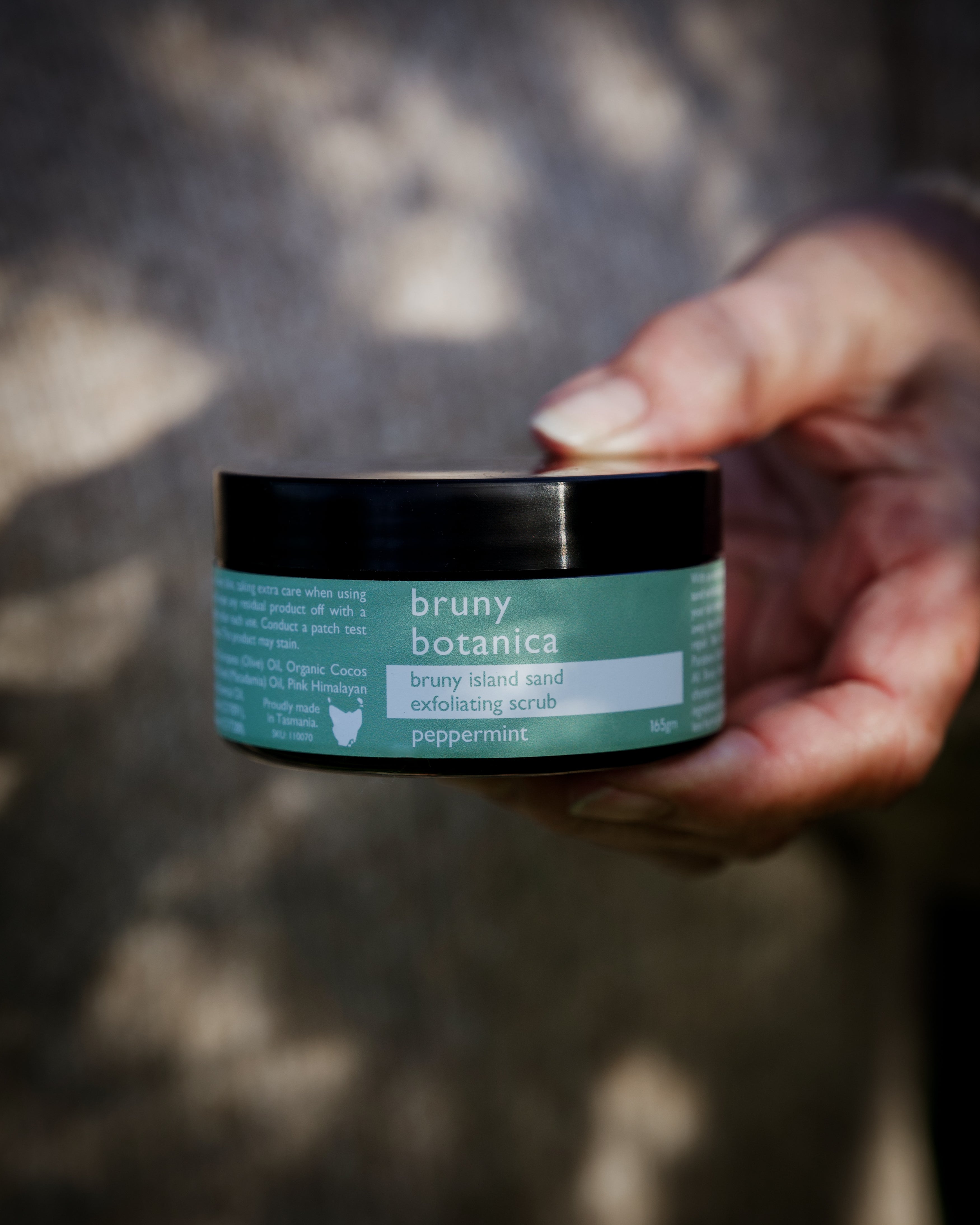 a hand holds the Bruny Island Sand Exfoliating Scrub - Peppermint out towards the camera