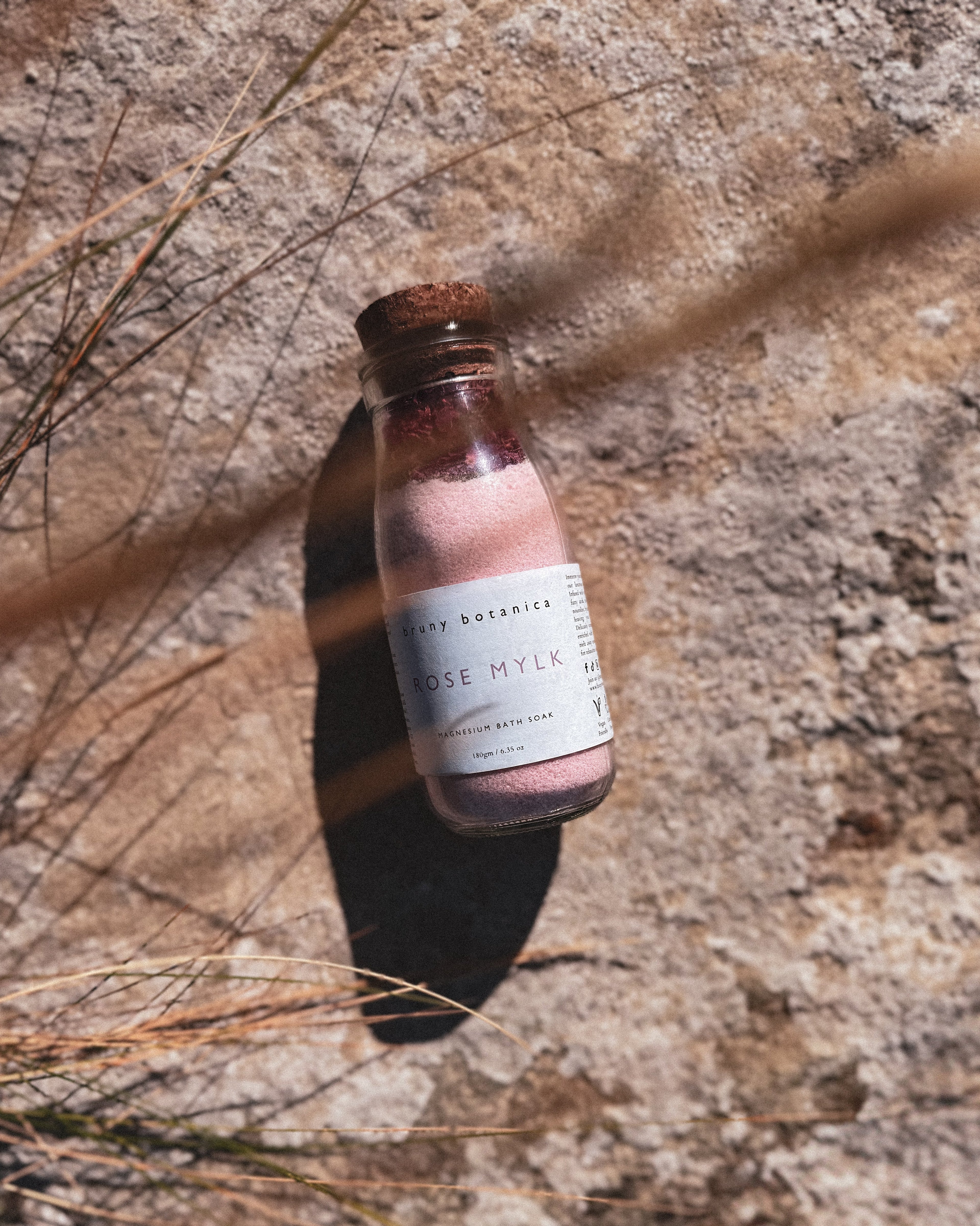A rose mylk magnesium soak sits against a rock background